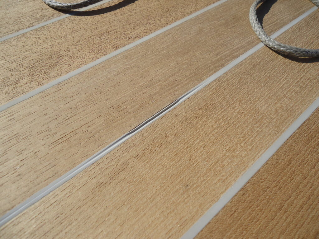 Image of teak deck with gray caulking that has been sanded too early and seam is deformed and separating