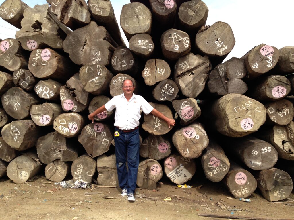 teak decking systems employee standing in front of Burmese teak logs in Myanmar