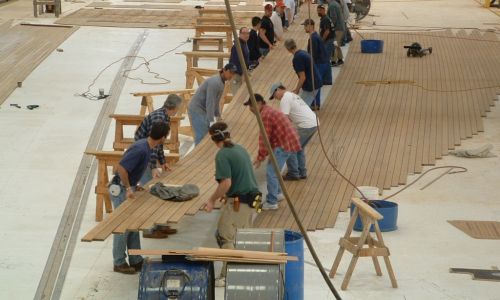 More than 20 employees lifting a large teak deck panel